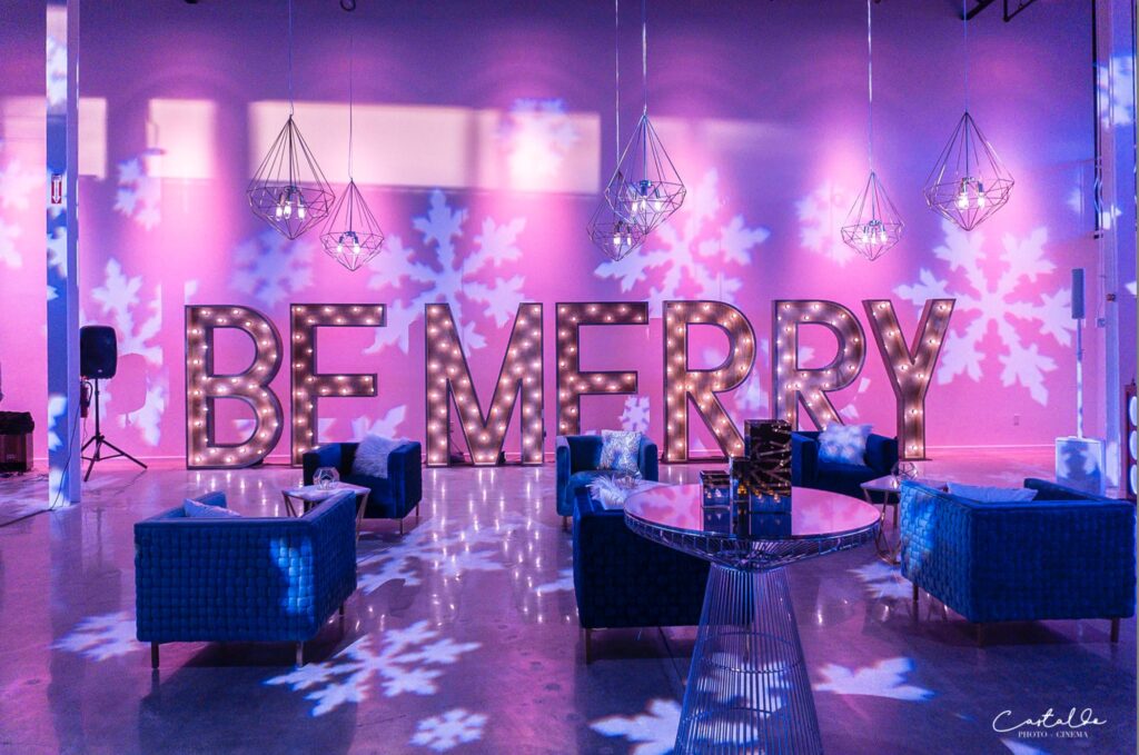 event space with blue chairs, pink lighting, and Be Merry sign with snowflake lights